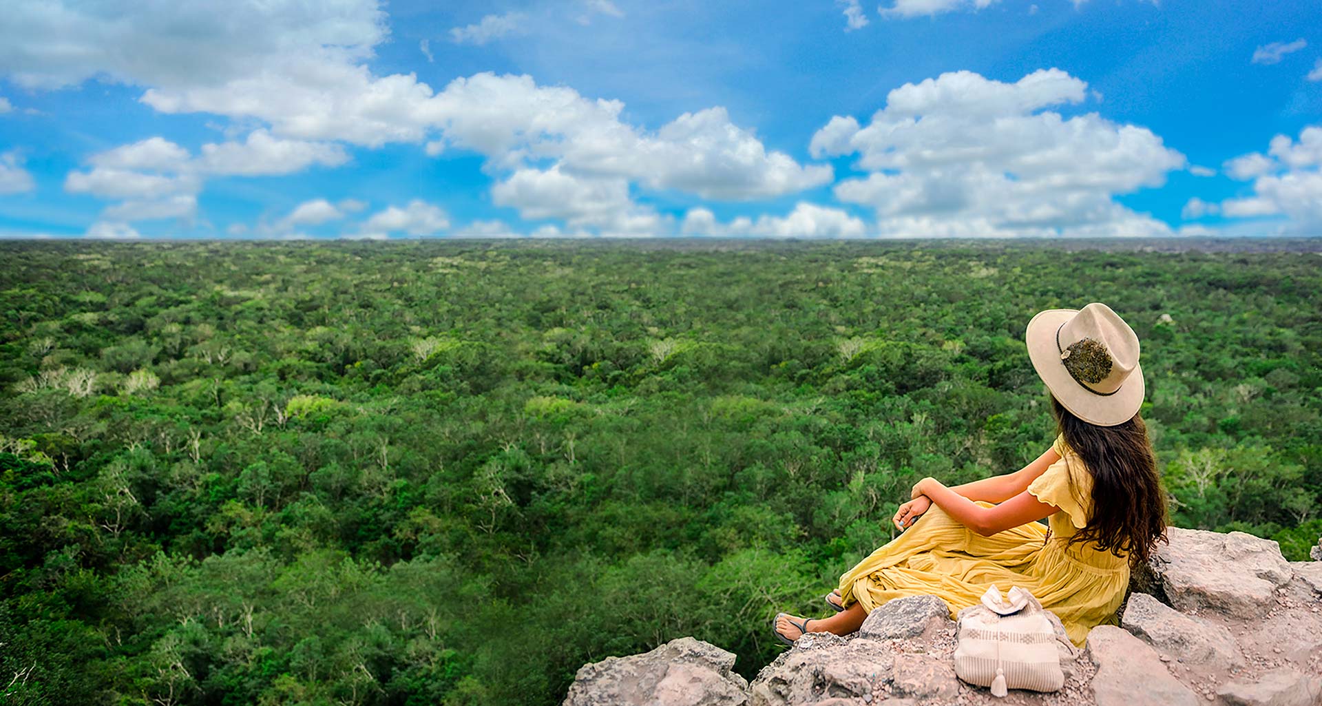young girl in a yellow dress with a hat looking to the jungle at the top of Coba pyramid